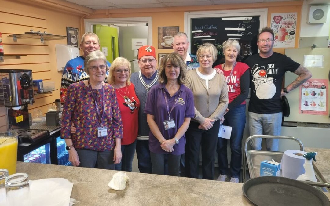 a group of volunteers are gathered for a photograph. many of them are wearing Christmas jumpers and they are smiling.