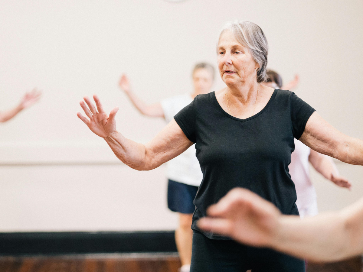 An older lady taking part in dance fit with outstretched arms